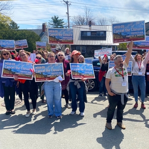Large group of people outside holding signs "Cancel the Closure"