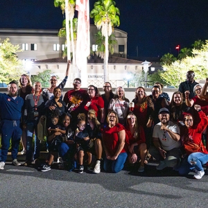 Large group of nurses outside hospital, smiling, with raised fists
