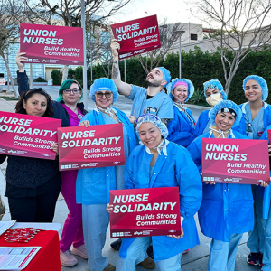 Group of nurses outside hospital, holding signs "Union Nurses" and "Nurse Solidarity"