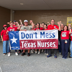 Large group of nurses outside hospital, with raised fists, holding banner "Don't Mess With Texas Nurses"