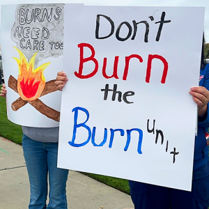Nurses holding signs "Don't burn the burn unit" and "Burns need care too"
