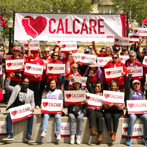 Large group of people outisde, holding CalCare signs and banner