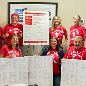 Group of nurses inside, smiling, holding large print outs of petition signer lists