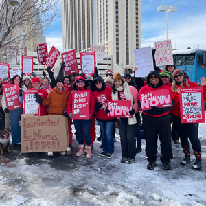 Large group of nurses outside hospital, in cold weather clothes, holding signs including "Safe Staffing NOW" and "Recruit, Retain, Respect RNs"