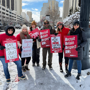 Group of nurses outside in cold weather clothes holding signs "Recruit, Retain, Respect RNs" and "Safe Staffing Saves Lives"