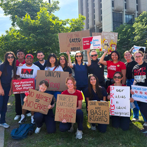 Large group of nurses outside holding signs calling for union rights, patient care, and an end to hospital greed