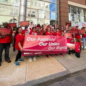 Group of nurses outside, holding banner "Our Patients, Our Union, Our Rights" and signs "Union Busting is a Sin"