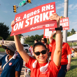 Nurse outside hospital holding sign "St. Agnes RNs ON STRIKE"