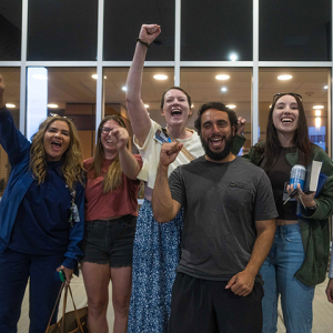 Group of six nurses outside hospital, smiling, with raised fists