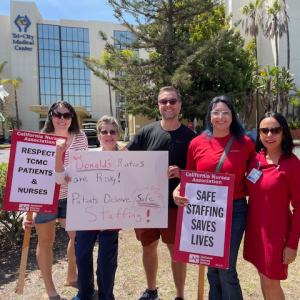Six nurses standing outside hospital smiling, holding signs "Safe Staffing Saves Lives" and "Respect TCMC Patients and Nurses"