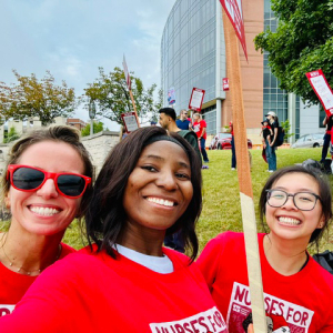 3 nurses outside hospital smiling, wearing red