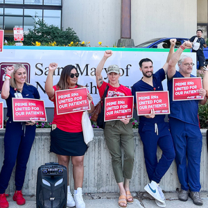 Nurse on picket line outside hospital holding signs "Prime RNs United for our Patients"
