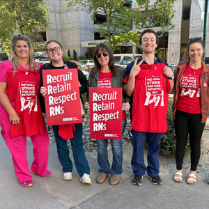 Five nurses outside, smiling, holding signs "Recruit, Retain, Respect RNs"