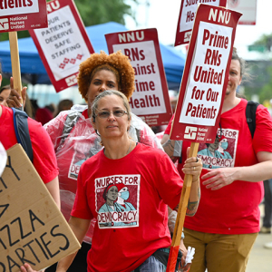 Nurse on picket line holding signs "Prime RNs United for our Patients"