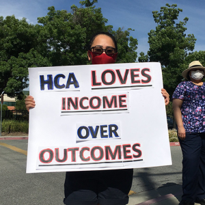 Nurses holds sign "HCA Loves Income Over Outcomes"
