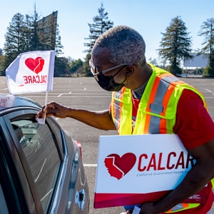 Person holding heart CalCare sign and placing flag on car.