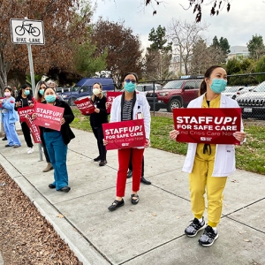 Group of four nurses outside hold signs "Staff up for safe patient care"