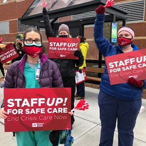 Group of four nurses outside hold signs "Staff up for safe patient care"
