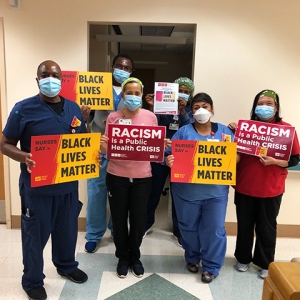Group of nurses inside hospital hold signs "Nurses Say: Black Lives Matter" and "Racism is a Public Health Crisis"