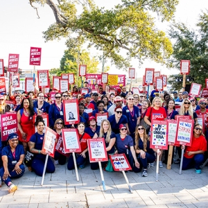 Very large group of nurses grouped outside hospital holding signs about going on strike