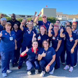 Large group of nurses outside hospital, smiling, with raised fists