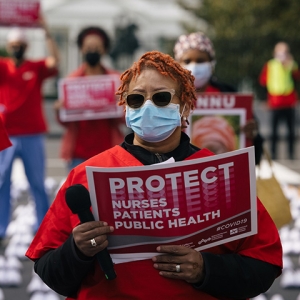 Masked nurse outside holds signs "Protect Nurses, Patients, Public Health"