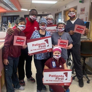 Large group of nurses inside hospital hold signs "Save Lives" and "Patients First"