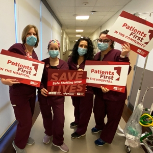 Four nurses holding signs in hospital hallway: "Patients First in the hospital" and "Save lives, safe staffng now"