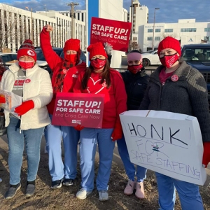 Group of four nurses outside hospital hold signs "Staff up for safe patient care"