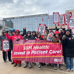 Group of nurses outside Saint Louis University Hospital holding banner "SSM Health: Invest in Patient Care!"