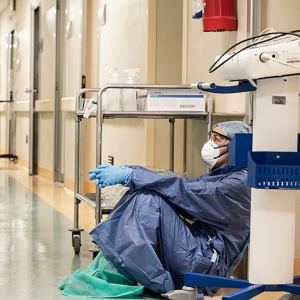 Exhausted nurse sitting on the floor of a hallway with medical equipment.