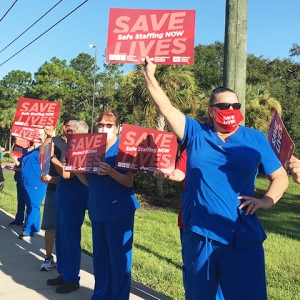 Nurses holding signs on sidewalk: "Save Lives, Safe Staffing NOW"