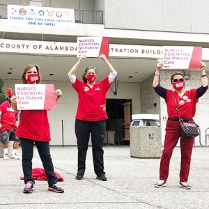3 nurses in front of Alameda facility holding signs: NURSES ESSENTIAL for Patient Care