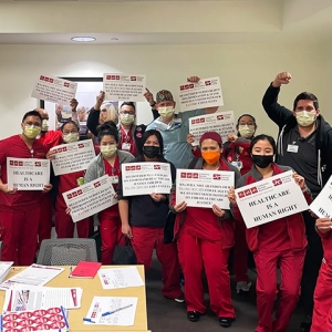 Large group of nurses inside hospital hold signs "Health care is a human right" with raised fists