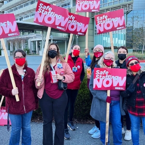 Group of nurses outside hold signs calling for safe staffing