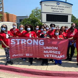 Large group of nurses outside hospital holding banner "Strong Union, Nurses, Veterans"