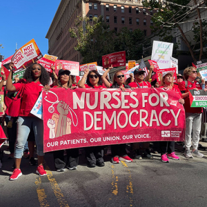 Nurse marching in street holding banner "Nurses for Democracy"