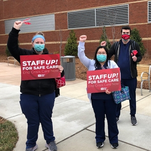 Nurses outside hospital hold signs "Staff Up for Safe Care"