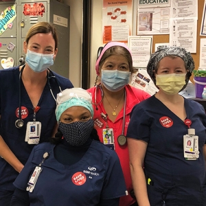 Group of four nurses inside hospital wearing stickers saying "Save Lives"