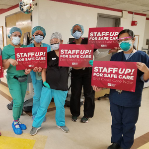 Large groups of nurses inside hospital hold signs "Staff Up for Safe Care"