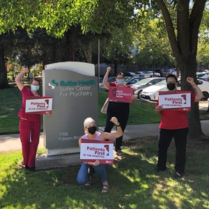 Group of nurses outside Sutter hospital with raised fists, holding signs "Patients First" and "Fair Contract Now"