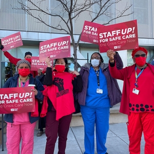 Group of nurses outside hold signs "Staff up for safe patient care"