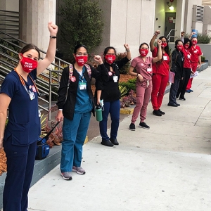 Group of nurses outside hospital with raised fists