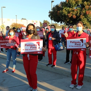 Large group of nurses outside hold signs "Patients First"