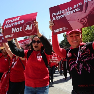 Nurses marching holding signs "Trust Nurses, Not AI" and "Patients Are Not Algorithms"