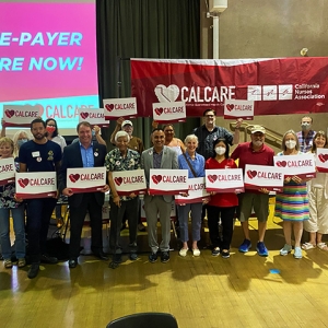 Large group of people standing in front of CalCare banner, holding CalCare signs