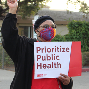 Nurse holds sign "Prioritize Public Health"