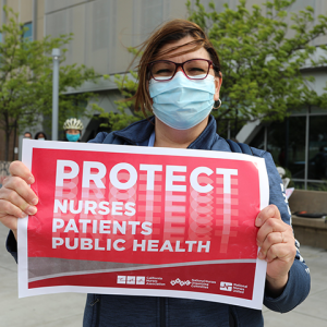 Nurse holds sign "Protect Nurses, Patients, Public Health"