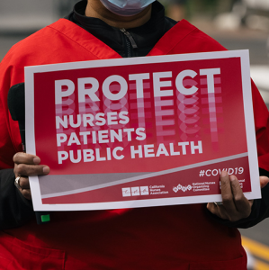 Nurse holds sign "Protect Nurses, Patients, Public Health"