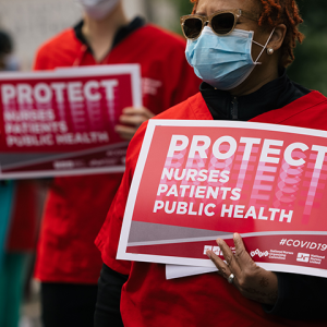 Nurse holds sign "Protect Nurses, Patients, Public Health"